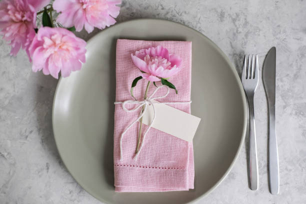 istock Mockup blank card for greeting or guest's name on the plate. Table setting with light green ceramic plates and pink peonies 1562939127