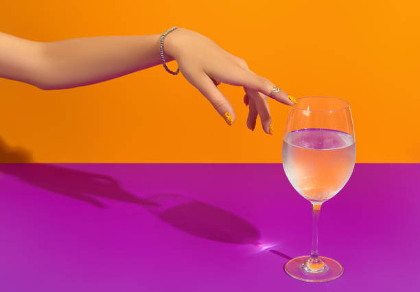 istock Womans hand touch glass on pink background. Manicure design trends 1562946458
