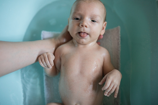 Portrait of cute newborn baby boy having a bath .He has a sweet and funny face with his tongue out.