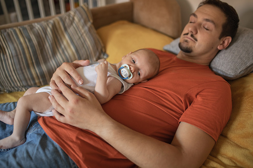 Cute newborn baby boy is laying on his father. They have a afternoon nap. Dad fell asleep first.