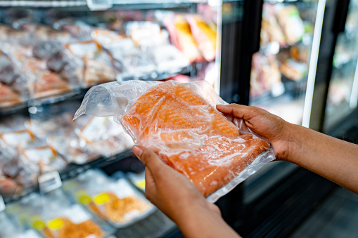 Close-up on a woman holding a fillet of salmon at the supermarket - grocery shopping concepts