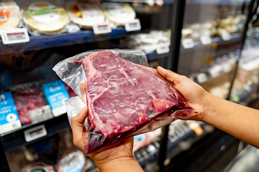 Close-up on a woman holding a raw steak at the supermarket while grocery shopping