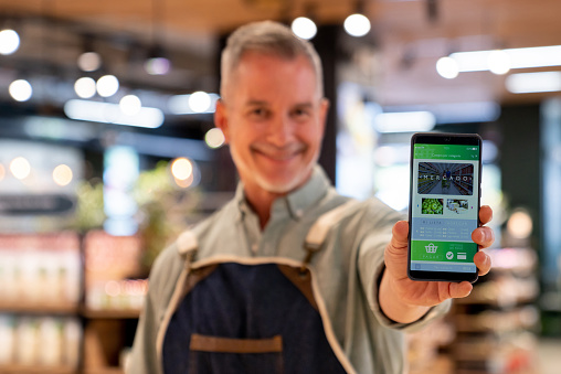 Portrait of a Latin American retail clerk showing a mobile app for online shopping on a cell phone