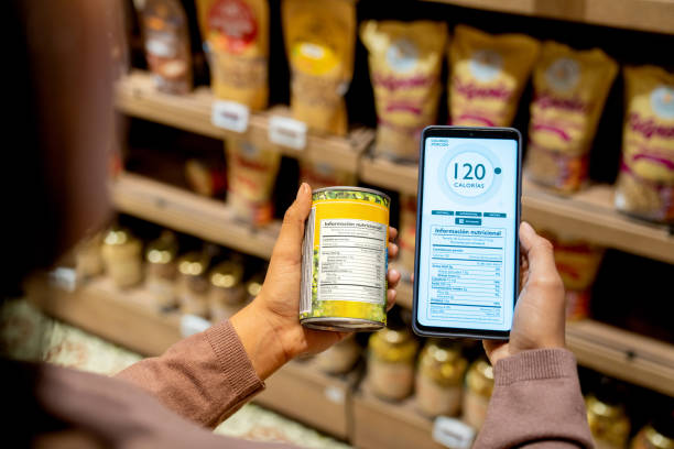 Woman scanning the nutrition label on a can at the supermarket Close-up on a woman scanning the nutrition label on a can at the supermarket while counting calories - healthy eating concepts grocery shelf cans stock pictures, royalty-free photos & images