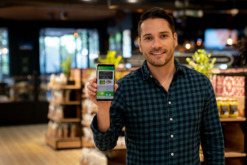 Portrait of a Latin American customer at the supermarket using an e-commerce app on his cell phone