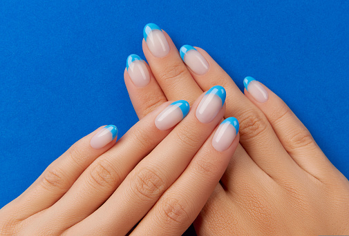 Beautiful womans hands trendy nail design on blue background. Manicure, pedicure beauty salon concept.