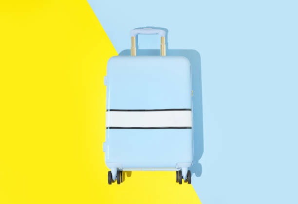 istock Suitcase on a blue yellow background with long deep shadows. Travel concept 1562970139