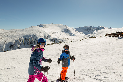 Two young children in ski gear on the top slopes of Borovets, Bulgaria. The mountain range in the background contains Musala, the highest peak in Bulgaria.
