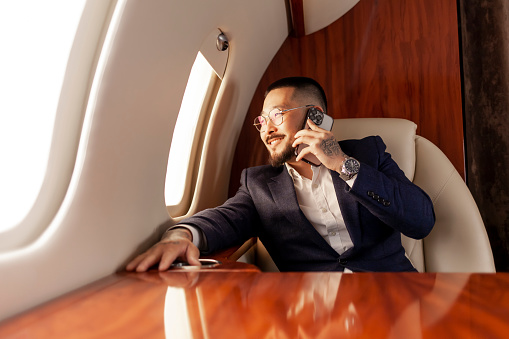 asian businessman in suit sits in private jet and talks on the phone, korean entrepreneur flies in airplane