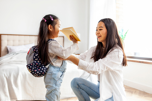 back to school, Asian little girl holding notebook at home in the morning, Korean woman helps her daughter get ready for school and puts her backpack on and supports the girl