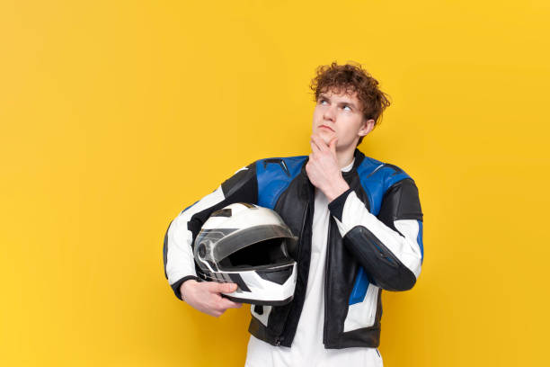 istock pensive guy motorcyclist in leather jacket holds helmet and thinks on yellow isolated background 1562972734