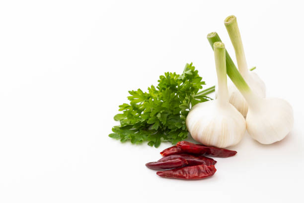 a bunch of fresh parsley, a metal scissor, cloves of garlic and hot peppers in the foreground, on a textured black background. View from above