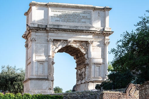 The Arch of Titus surrounded by lush green trees. Rome, Italy.