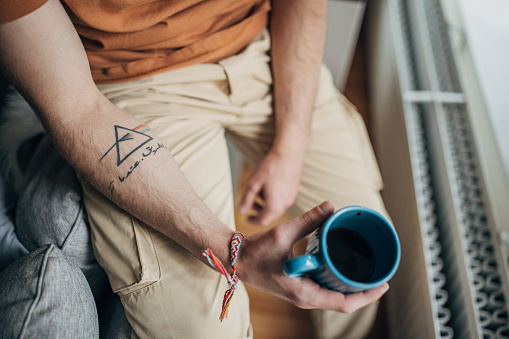 Unrecognizable man holding a cup of coffee while sitting at home.