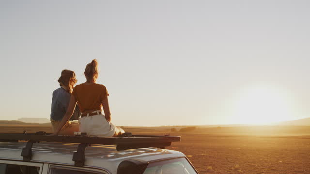 Travel, sunset in desert and women with camera on car roof, nature photography and trekking adventure. Road trip, photographer and lesbian couple on vehicle taking picture of safari view in evening.