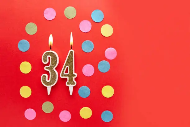 Number 34 on a red background with colored confetti. Happy birthday candles. The concept of celebrating a birthday, anniversary, important date, holiday. Copy space. banner