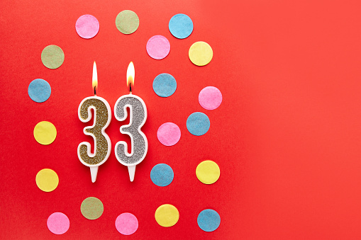 Number 33 on a red background with colored confetti. Happy birthday candles. The concept of celebrating a birthday, anniversary, important date, holiday. Copy space. banner
