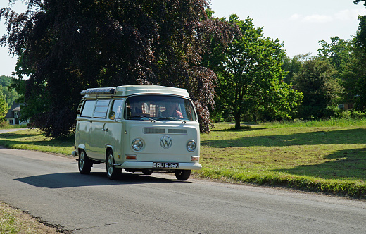 Ickwell, Bedfordshire, England - June  04, 2023: Classic  Volkswagen Camper Van driving though village cottage and trees in the background.
