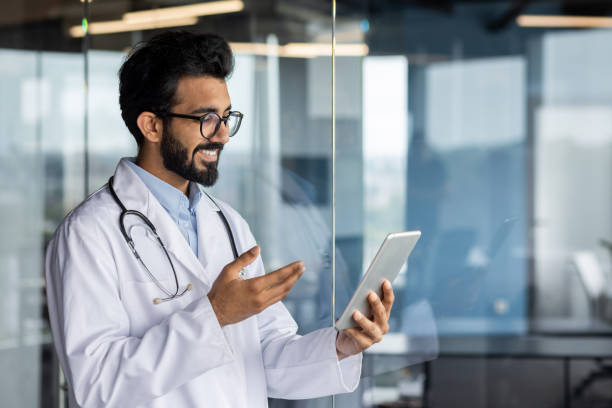 istock Successful professional Indian doctor working inside modern clinic, man consulting patients remotely, using tablet computer for video call, and long distance communication 1562983759