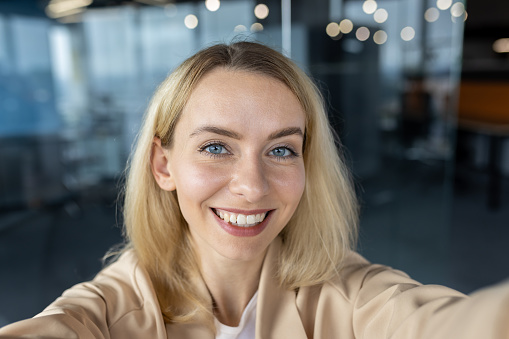 Close-up photo. Young businesswoman, designer standing in the office and taking a selfie, talking on a video call from the phone, smiling at the camera.