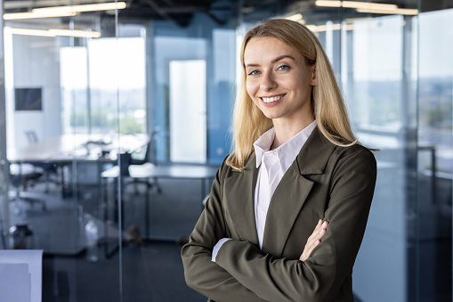 Portrait of a successful and smiling business woman, the founder of the company, the director in a suit standing confidently in the office. crossing his arms on his chest, looking at the camera.