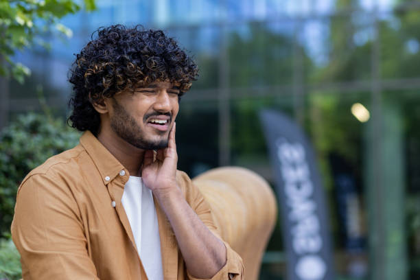 istock A young hispanic man sits outside on a bench, grimacing and holding a hand to his cheek. Suffering from toothache. Close-up photo 1562985404