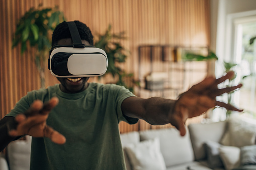 Black man having fun with virtual reality headset in living room at home.