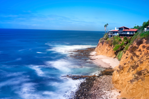 A scenic shot of a cliffside home that overlooks the rugged ocean.  Image was created in camera using a slow shutter speed to capture the motion of the water.
