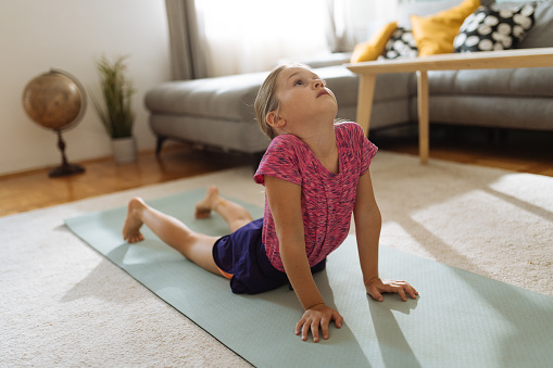 Preschool girl exercising at home on yoga mat