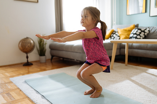 Preschool girl exercising at home on yoga mat