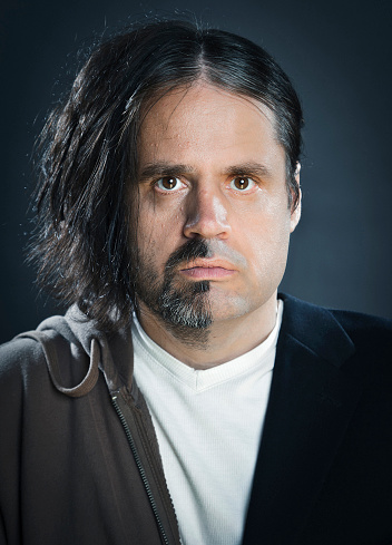 A portrait of a man. On one side he has long hair and is unshaven, and on the other side he is clean shaven with short hair. 