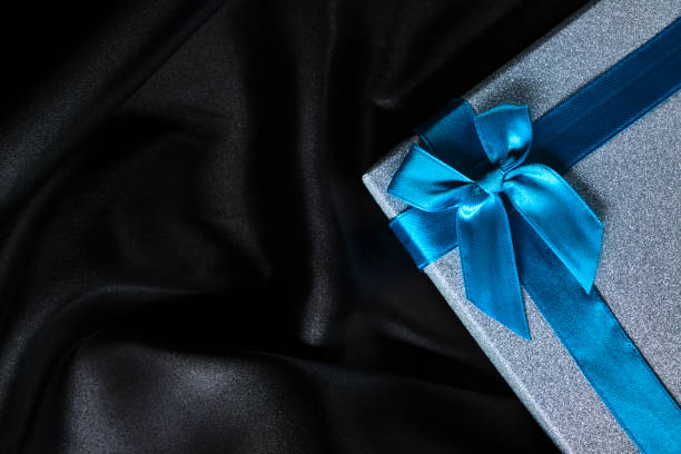 istock Silver gift box with blue bow background black silk fabric. 1563031739