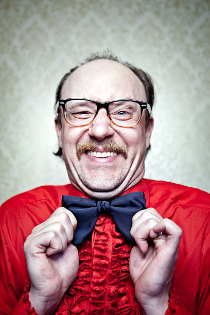 Crazy Butler Man in Red Frilly Shirt & Bow Tie A balding man in a retro frilly red tuxedo shirt, mustache, and glasses, makes a goofy face while straightening his bow tie.  Vintage damask pattern wallpaper on wall in the background.  Vertical with copy space. bow tie photos stock pictures, royalty-free photos & images