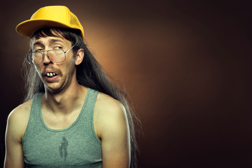 A profile portrait of an uncertain or sad hillbilly man with a long flowing mullet, mustache, trucker hat,  and rotten teeth.  Brown background; horizontal with copy space.