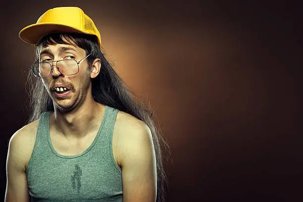 A profile portrait of an uncertain or sad hillbilly man with a long flowing mullet, mustache, trucker hat,  and rotten teeth.  Brown background; horizontal with copy space.
