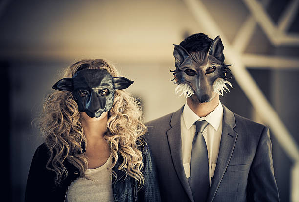 young couple wearing animal mask young couple with animal mask (male as wolf - female as a sheep) wearing business like attire posing against a light shaded background animal representation photos stock pictures, royalty-free photos & images