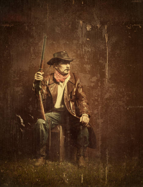 Adult serious cowboy sitting on a haystack took out his revolver