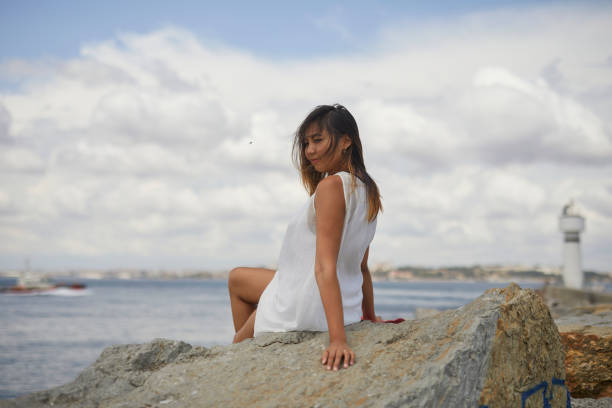 Beautiful Kazakh tourist girl sitting over rocks near lighthouse at Istanbul, with amazing old city in background