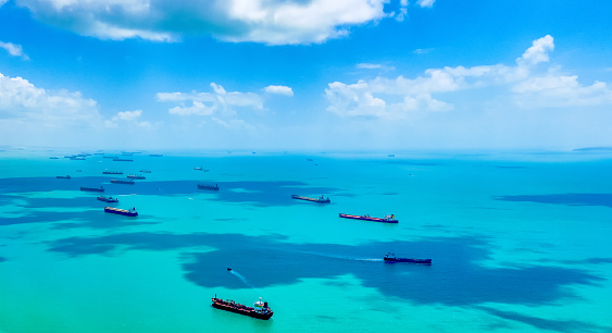 Aerial view of cargo, freight or container ships in the road in Singapore Strait. Blue sky, beautiful clouds, azure clear sea waters. Cargo ships anchored and waiting to enter the busiest port in South East Asia. Copyspace. International trade.
