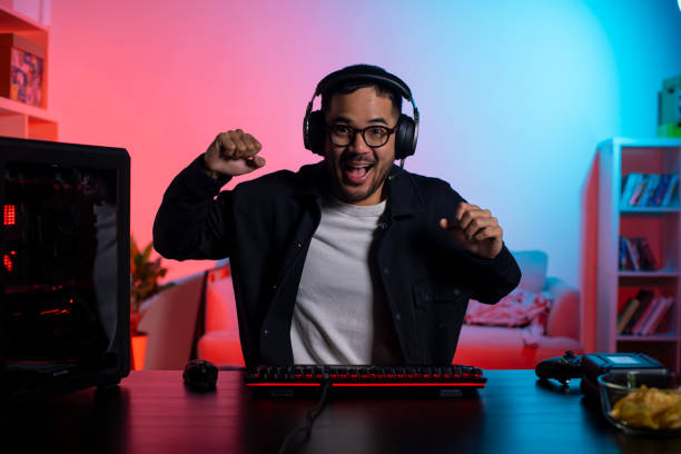 Happy young Asian man playing a video game, cheering after winning