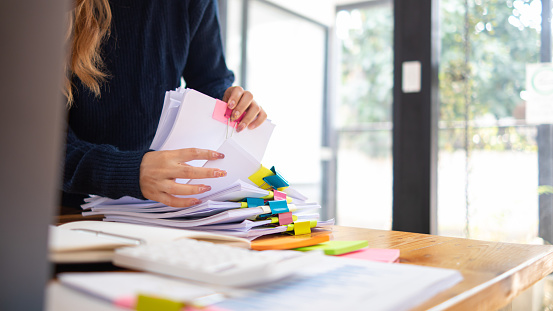 secretary searches through stacked paperwork on desk in office to find lease within stacked paperwork just before meeting. concept difficulty in finding hire purchase contract from stacked paperwork