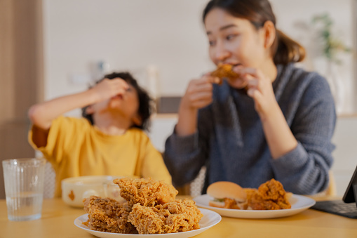 Asian boy eating fried chicken at the dining table.