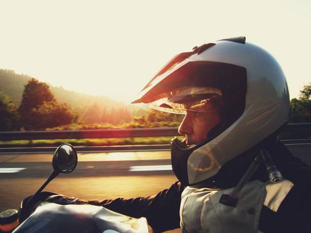istock Man wearing a silver helmet riding a motorcycle at sunset 156323194