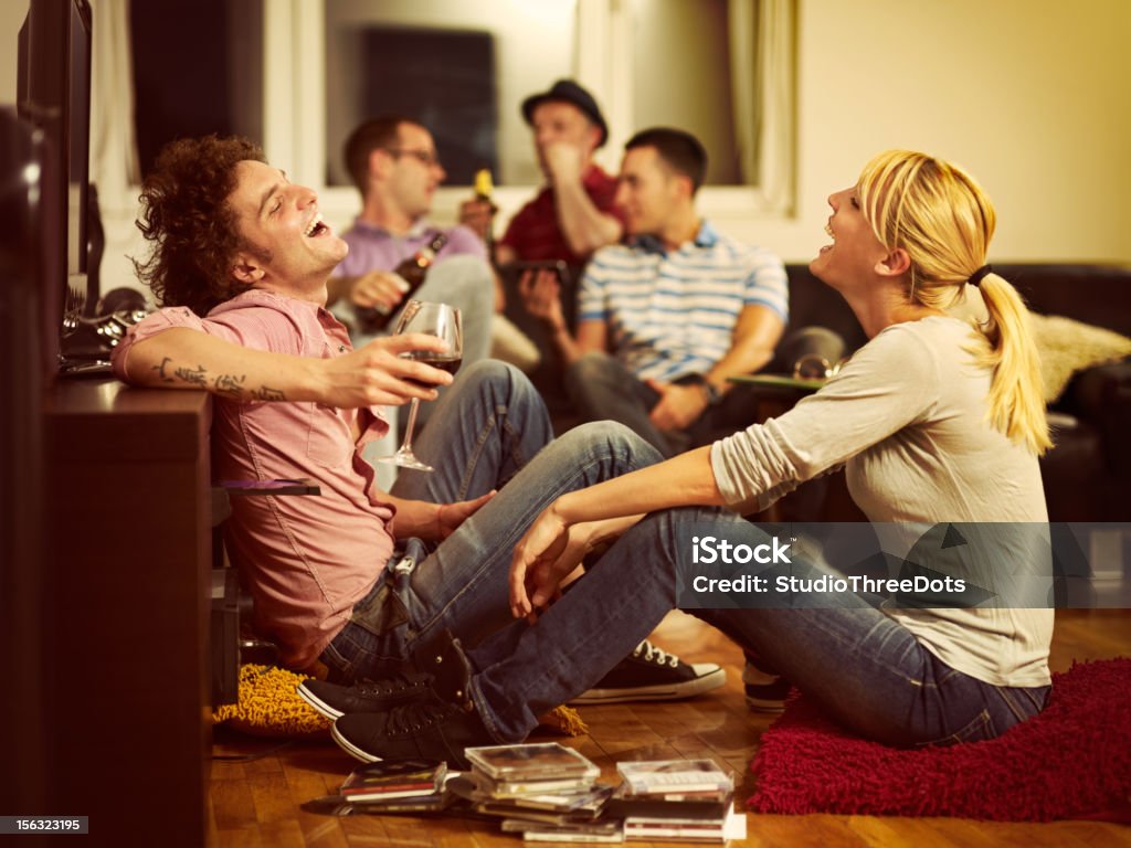 young couple sitting on the floor and watching TV young couple sitting on the floor and watching TV, woman is holding the cd cover Party - Social Event Stock Photo