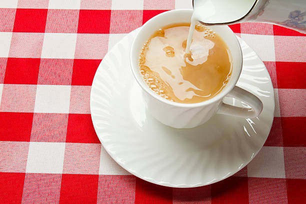 Milk mixing with hot tea in a white teacup on a saucer on a red checked gingham table cloth.  This type of tea is a classic afternoon refreshment all over Great Britain.