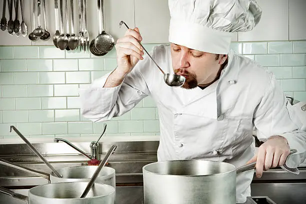 Young chef tasting soup in restaurant kitchen