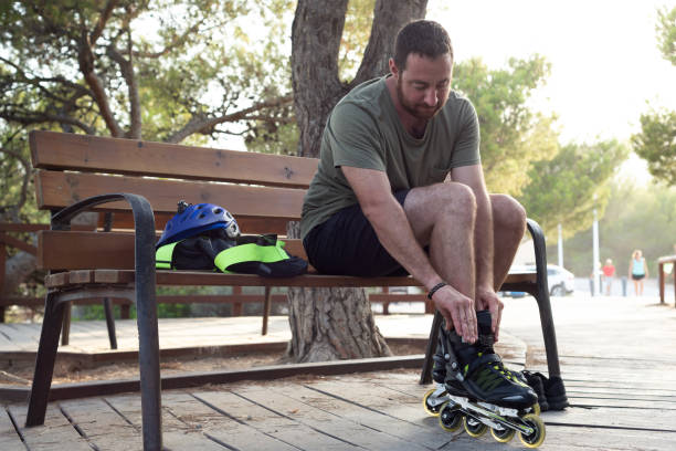 istock Man sitting on a wooden bench while putting on inline skates. 1563254780