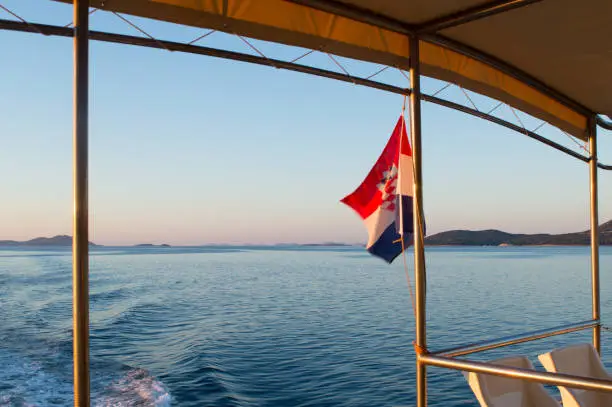 Croatian flag waving on a boat trip in Dalmatia during sunrise, Zadar region, Adriatic sea