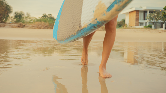 Closeup of Young Asian woman surfer runs with surfing board on tropical beach. Healthy active lifestyle and summer vacation concept.