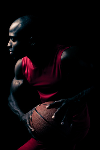 Dramatically lit, intense basketball player. Making a move to pass the ball.